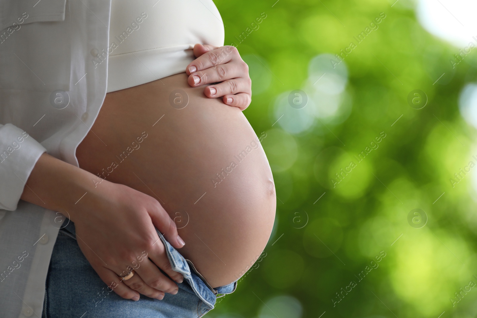 Image of Young pregnant woman touching her belly outdoors, closeup. Space for text