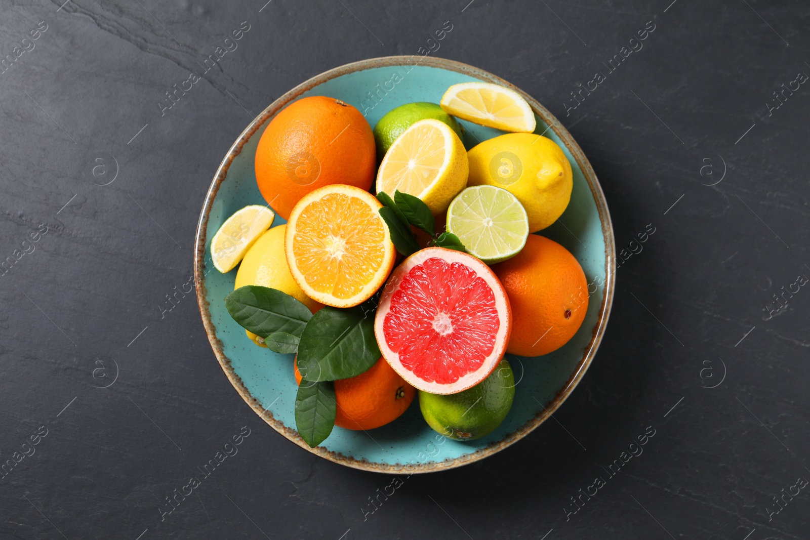 Photo of Different cut and whole citrus fruits on black table, top view