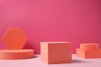 Photo of Many orange geometric figures on table against pink background, space for text . Stylish presentation for product