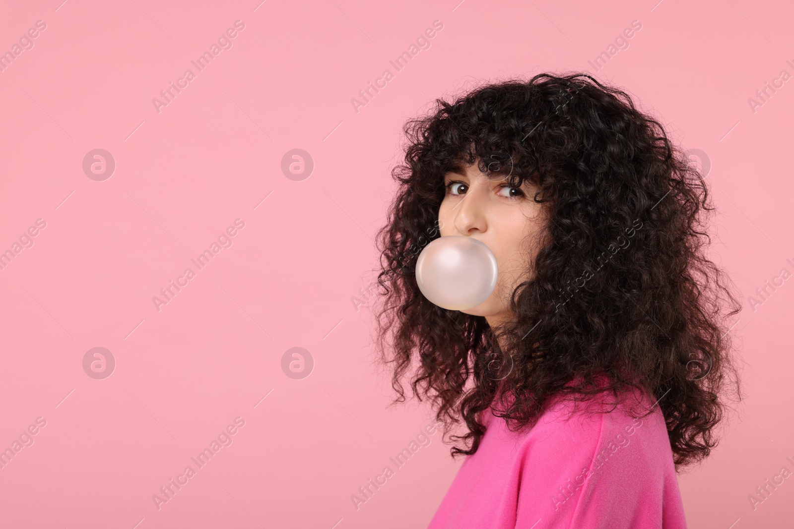 Photo of Beautiful young woman blowing bubble gum on pink background. Space for text