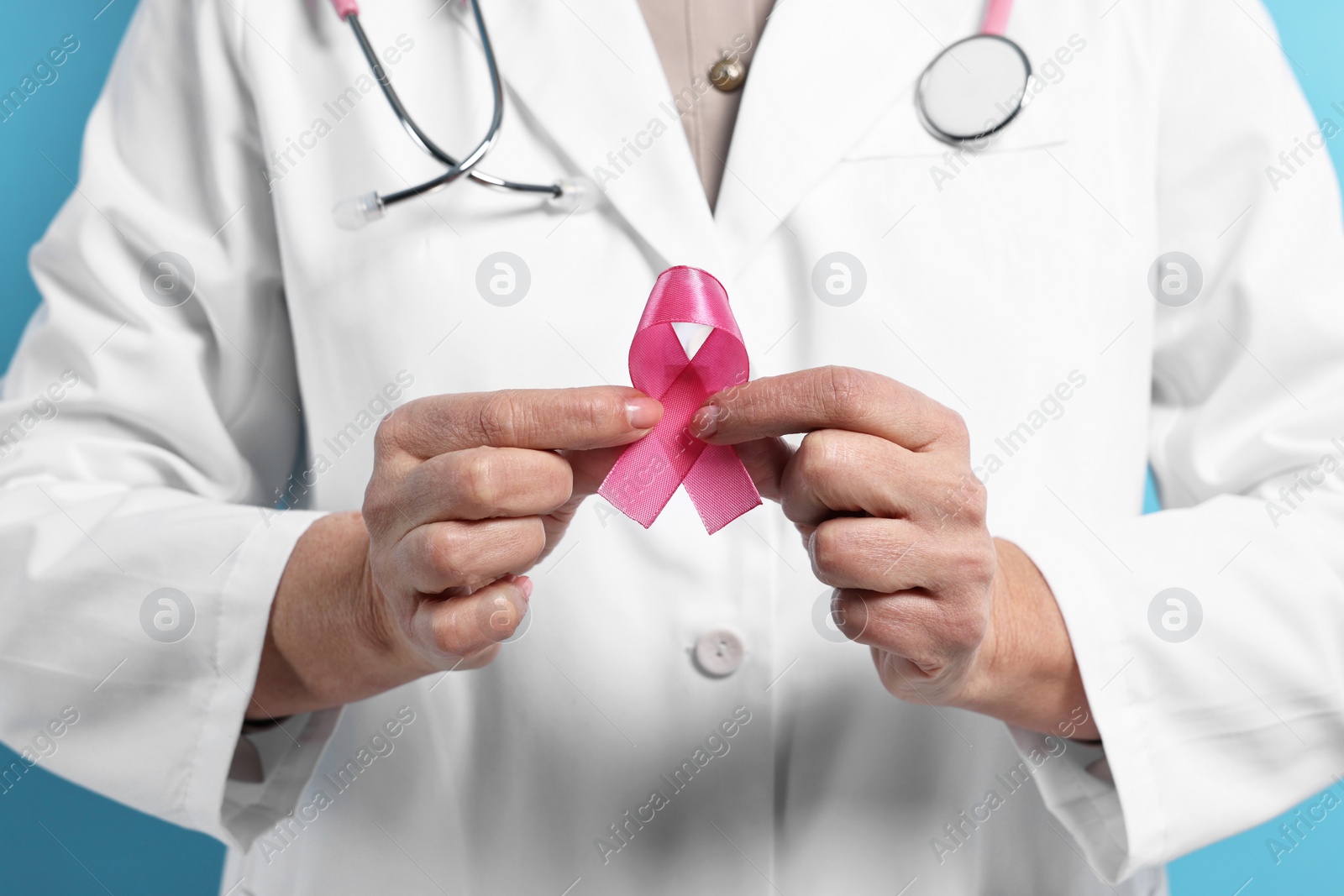 Photo of Mammologist with pink ribbon on light blue background, closeup. Breast cancer awareness