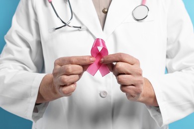 Photo of Mammologist with pink ribbon on light blue background, closeup. Breast cancer awareness