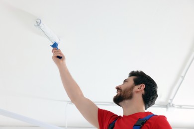Photo of Handyman painting ceiling with roller in room, low angle view