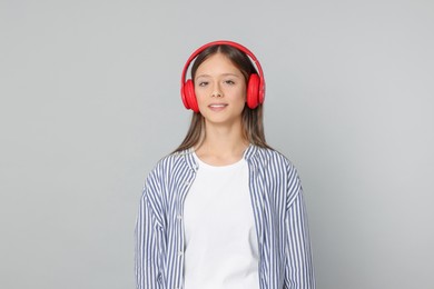 Photo of Teenage girl listening to music with red headphones on light grey background