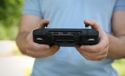 Photo of Man holding new modern drone controller outdoors, closeup of hands