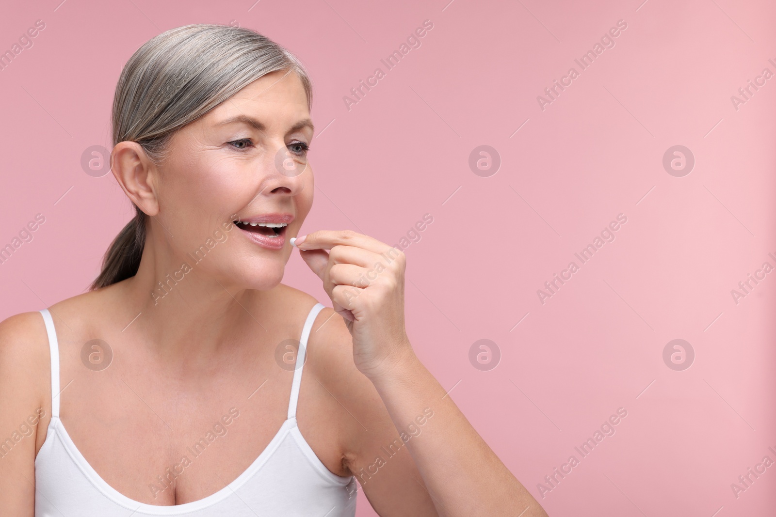 Photo of Beautiful woman taking vitamin capsule on pink background, space for text
