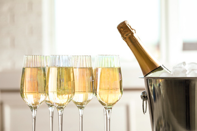 Photo of Glasses of champagne and ice bucket with bottle on blurred background