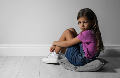 Sad little girl near white wall, space for text. Domestic violence concept