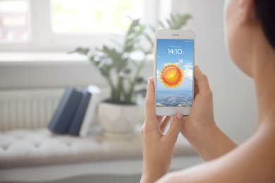 Woman using weather forecast app on smartphone indoors, closeup. Space for text