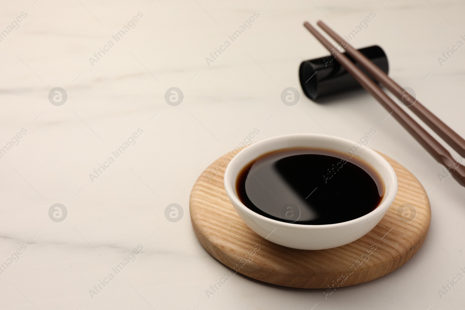 Photo of Bowl with soy sauce and chopsticks on white marble table. Space for text
