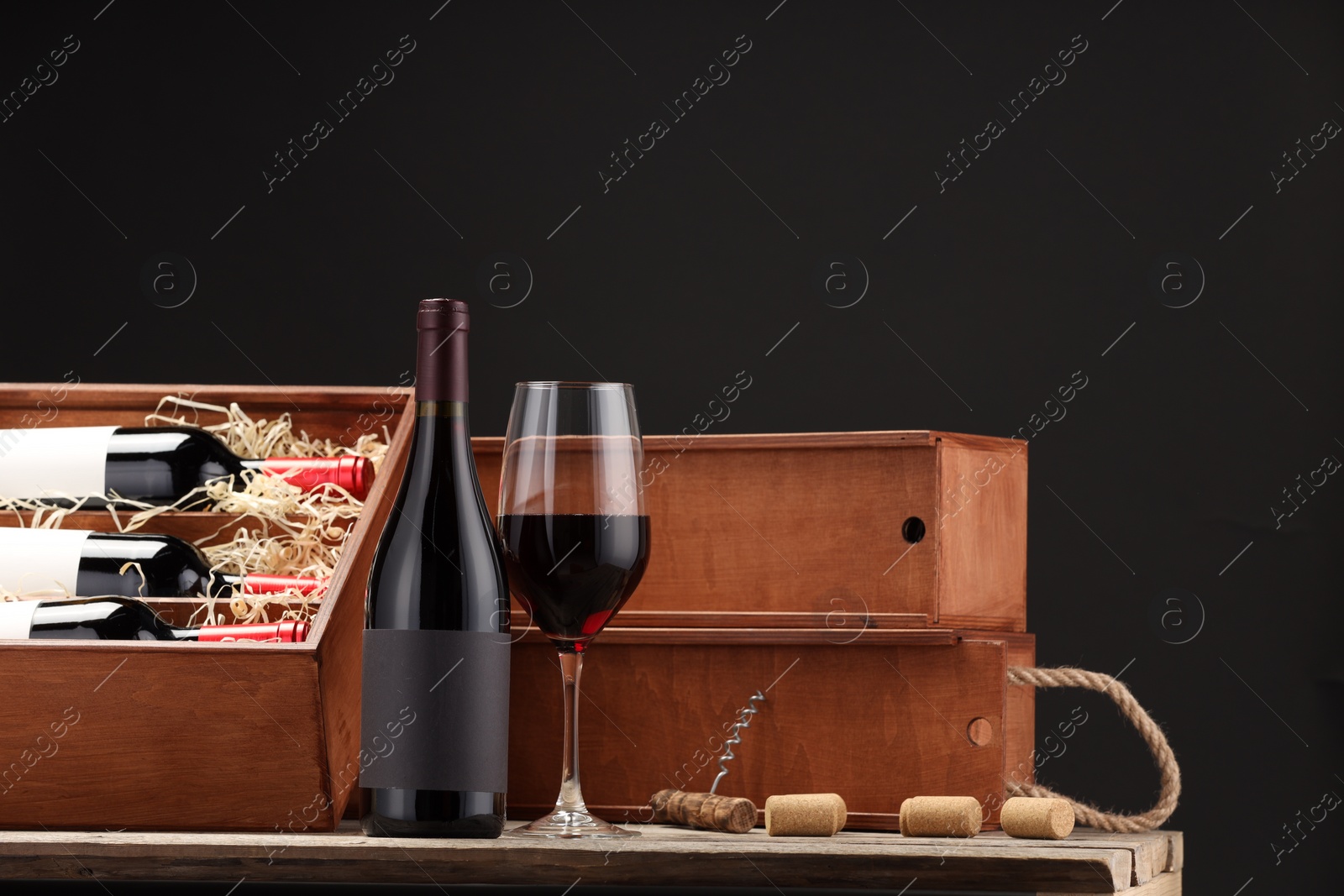 Photo of Box with wine bottles, glass, corks and corkscrew on wooden table against black background