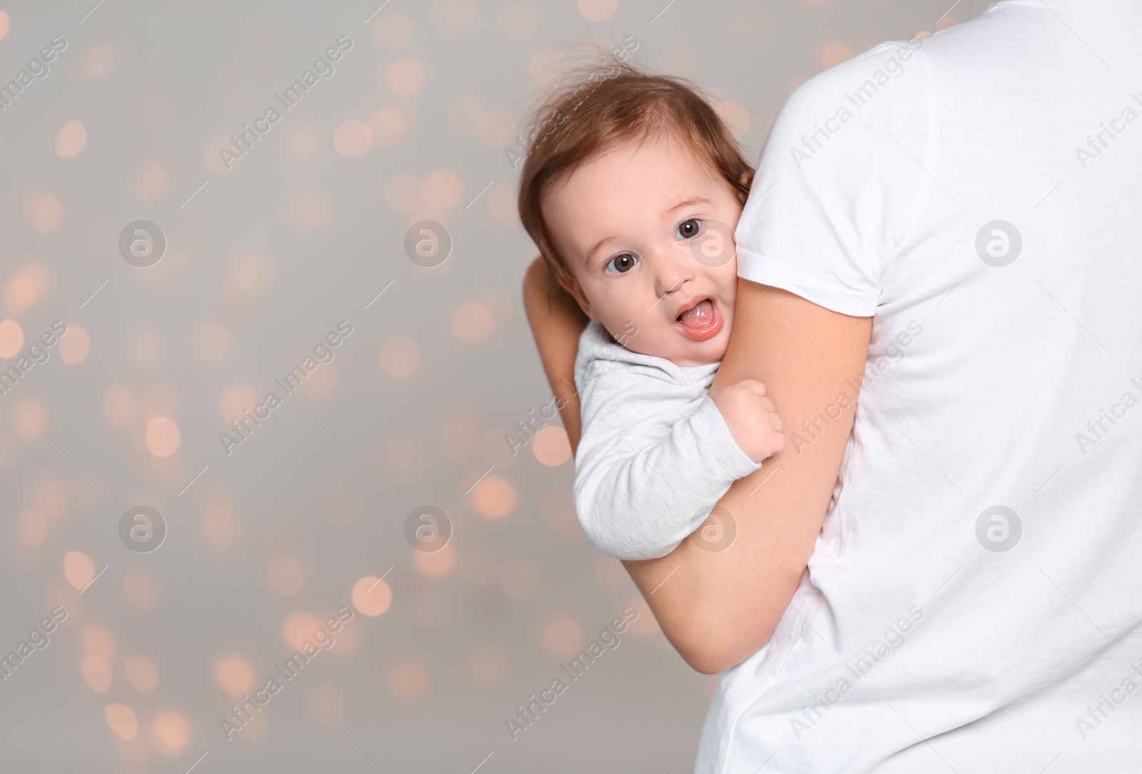 Photo of Young mother holding cute baby against  defocused lights. Space for text