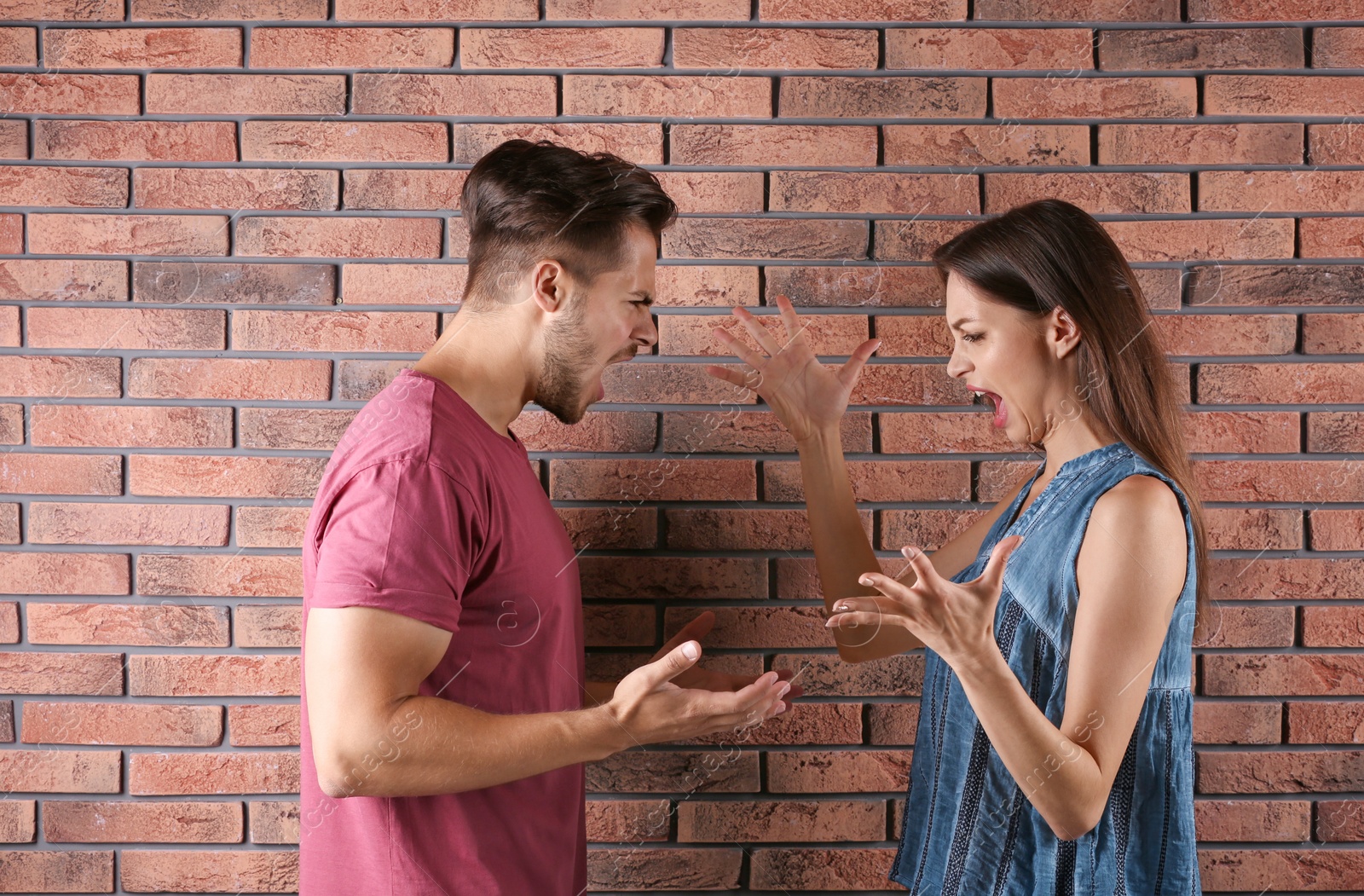 Photo of Young couple having argument near brick wall. Relationship problems