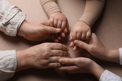 Photo of Family holding hands together on brown background, above view