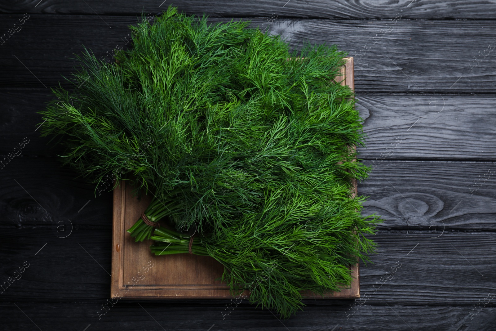 Photo of Bunches of fresh dill on black wooden table, top view