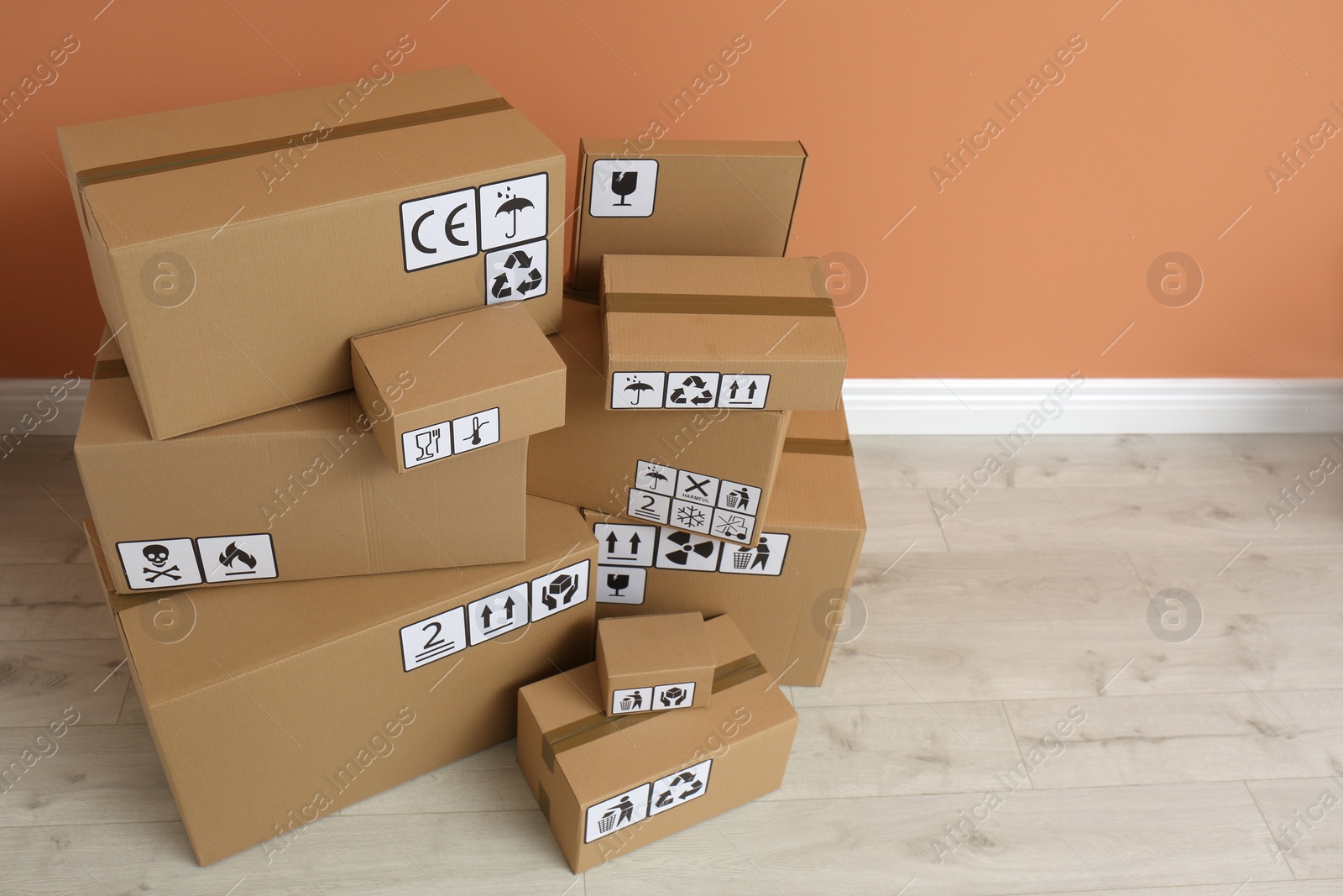 Photo of Cardboard boxes with different packaging symbols on floor near orange wall. Parcel delivery