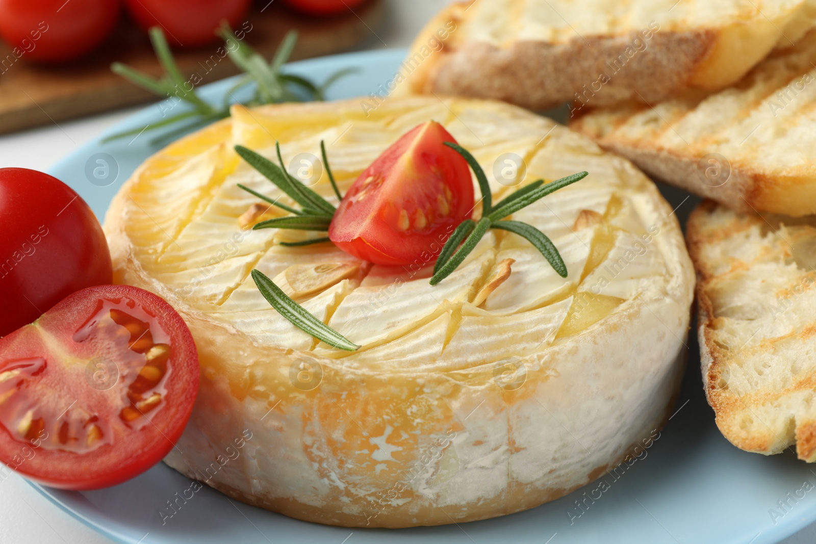 Photo of Tasty baked brie cheese with rosemary and cherry tomatoes on plate, closeup