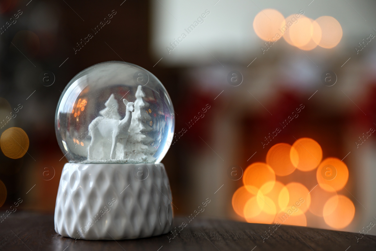 Photo of Snow globe on wooden table against blurred background, space for text. Bokeh effect