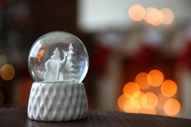 Snow globe on wooden table against blurred background, space for text. Bokeh effect