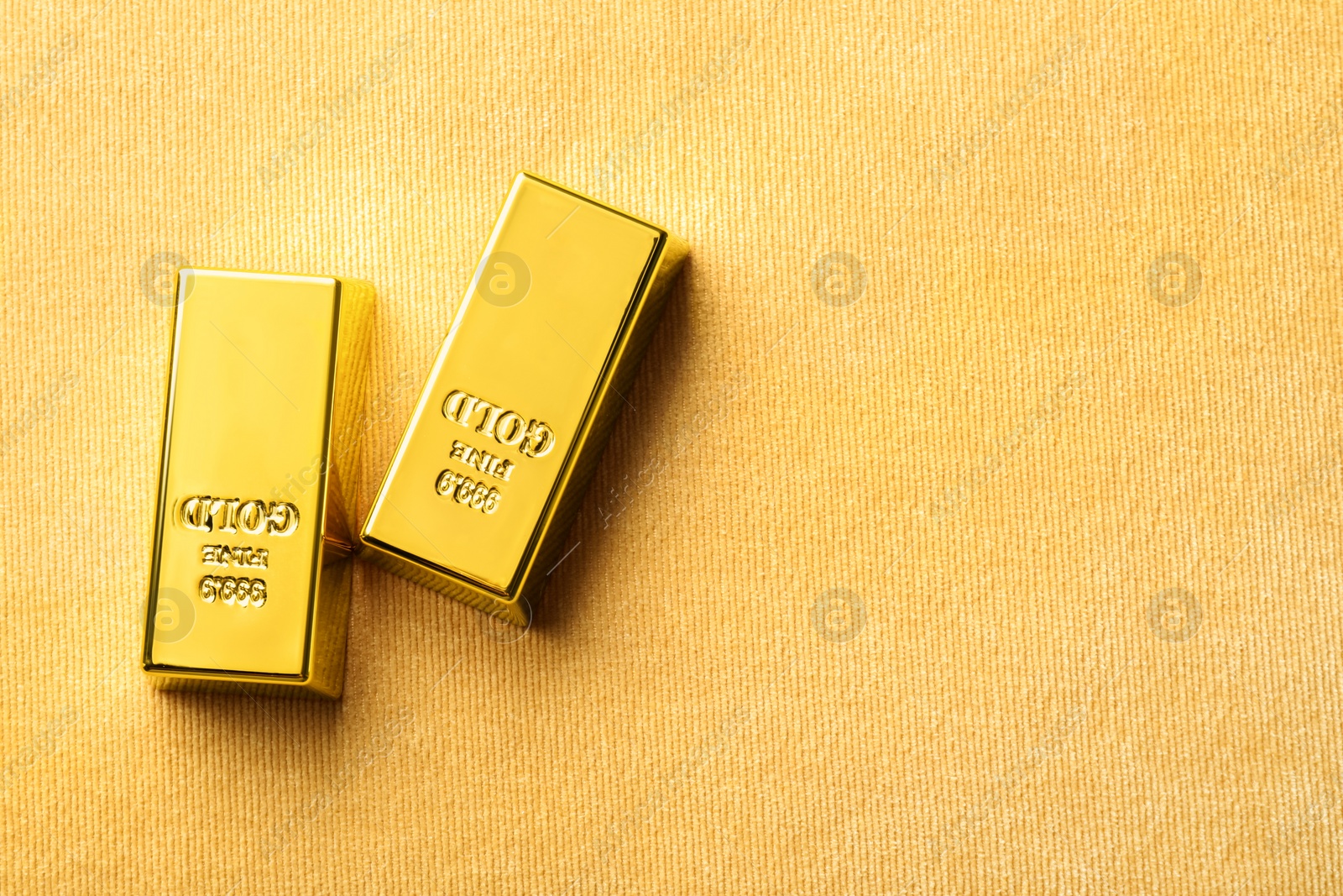 Photo of Many shiny gold bars on yellow fabric, flat lay. Space for text