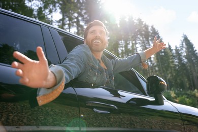 Enjoying trip. Happy man leaning out of car window on sunny day, low angle view