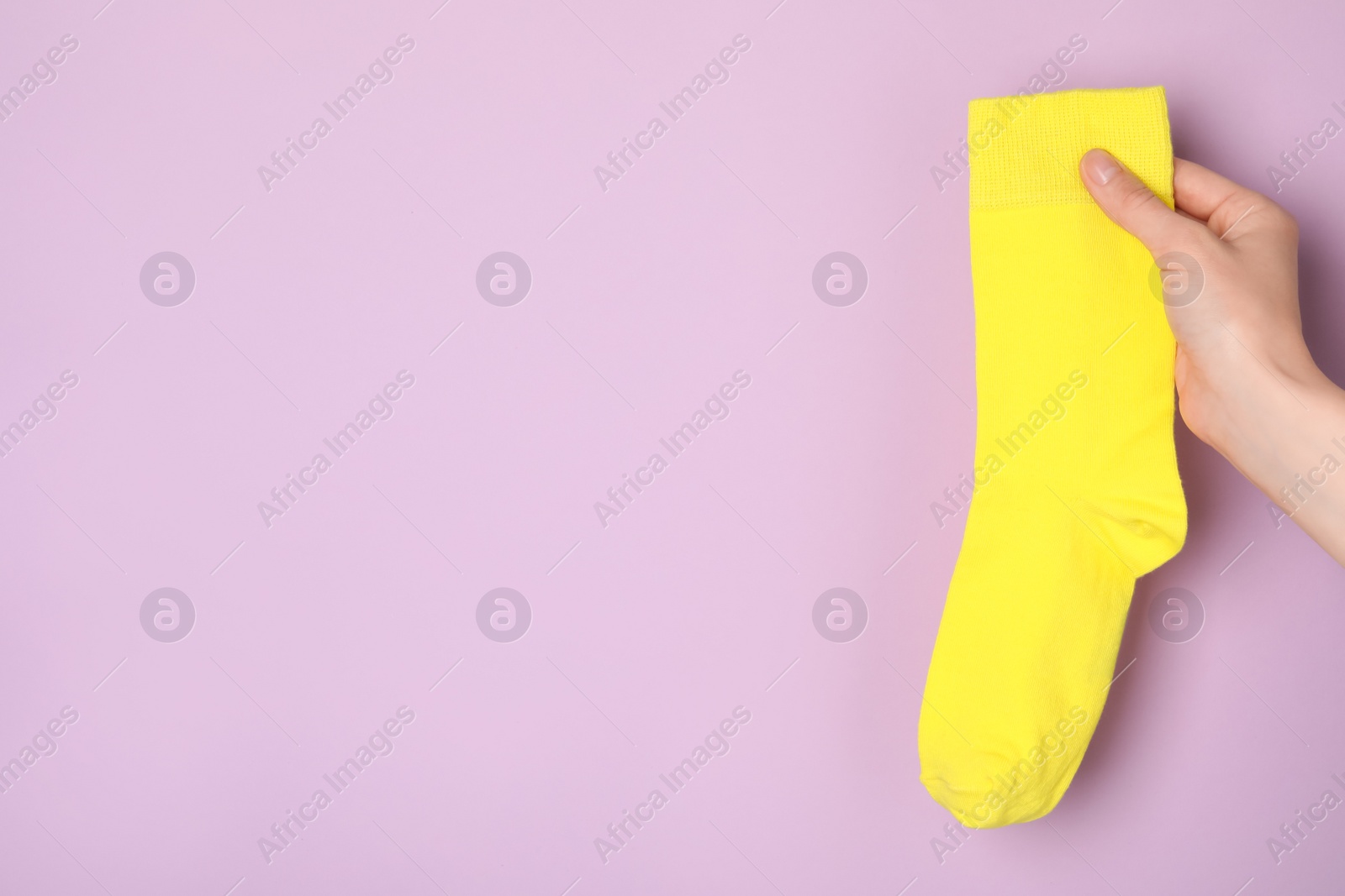 Photo of Woman holding yellow sock on light violet background, closeup. Space for text
