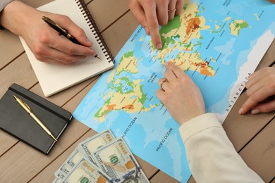 Man and woman planning their honeymoon trip with world map at wooden table, top view