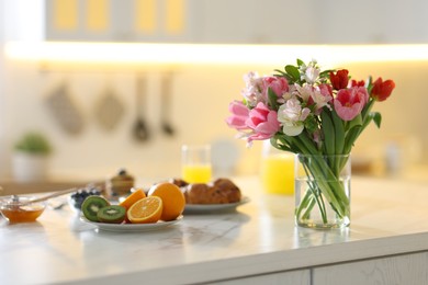 Bouquet of beautiful flowers in vase and food for breakfast on white table