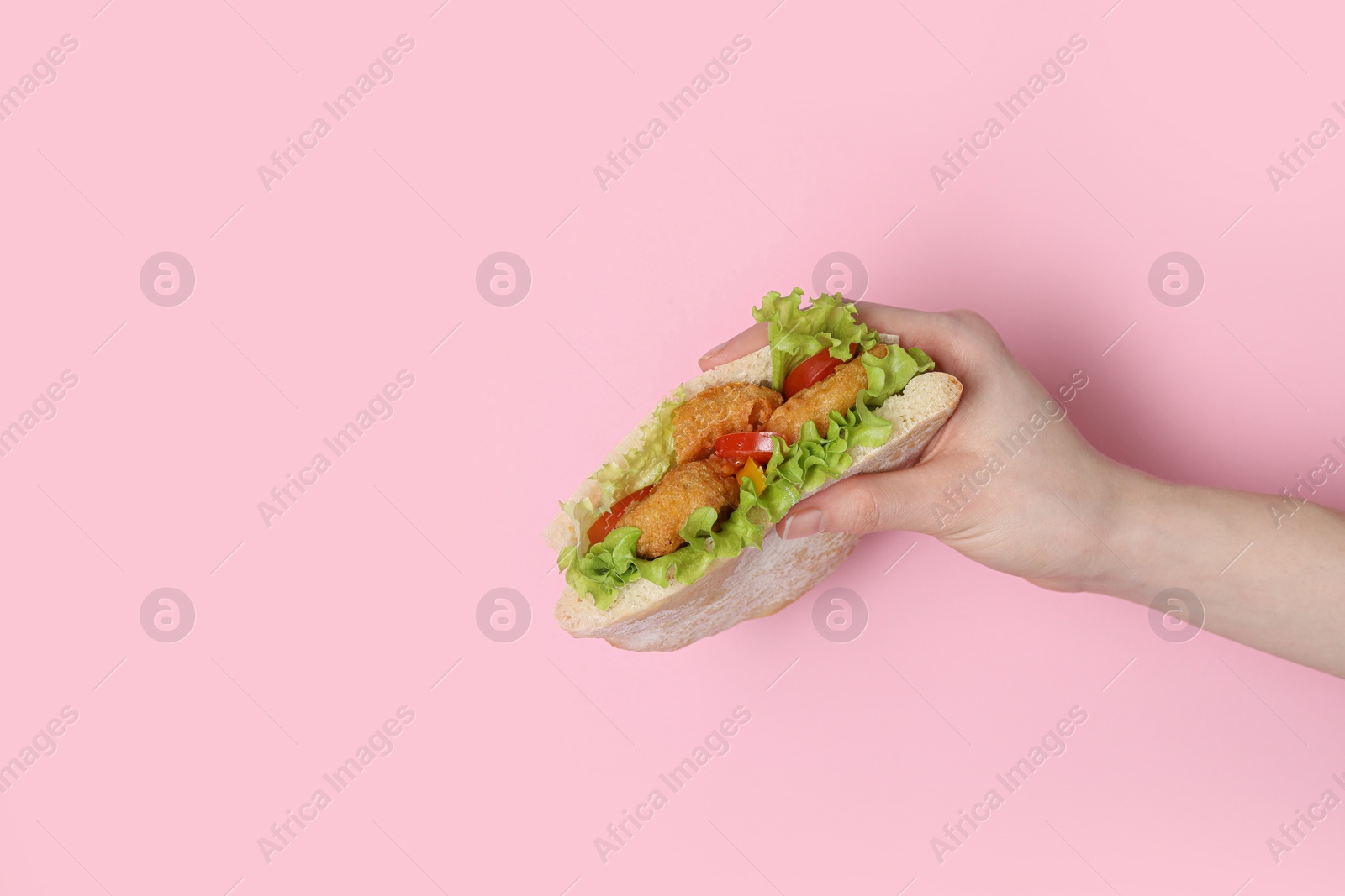 Photo of Woman holding delicious pita sandwich with fried fish, pepper, tomatoes and lettuce on pink background, closeup. Space for text