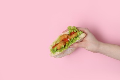 Woman holding delicious pita sandwich with fried fish, pepper, tomatoes and lettuce on pink background, closeup. Space for text