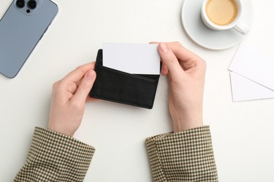 Photo of Woman holding leather business card holder with blank card at white table, top view