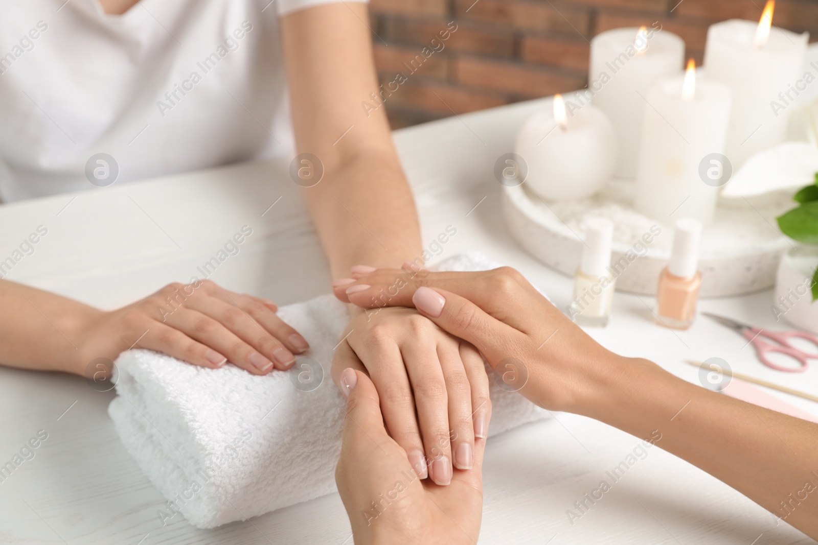 Photo of Cosmetologist massaging client's hand at table in spa salon, closeup