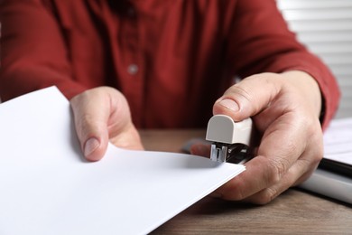 Photo of Man with papers using stapler at wooden table, closeup