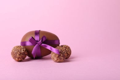 Photo of Tasty chocolate egg with purple bow and candies on pink background. Space for text
