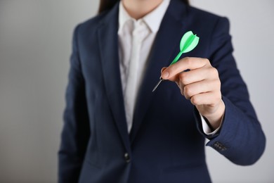 Businesswoman holding green dart on light background, closeup