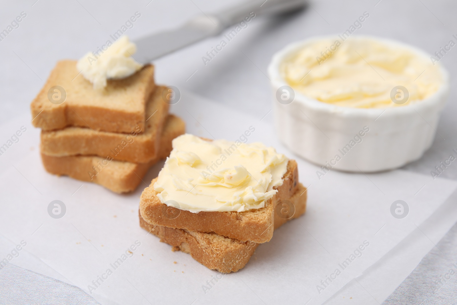 Photo of Slices of bread with tasty butter and knife on light table, closeup