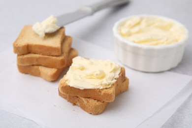 Slices of bread with tasty butter and knife on light table, closeup