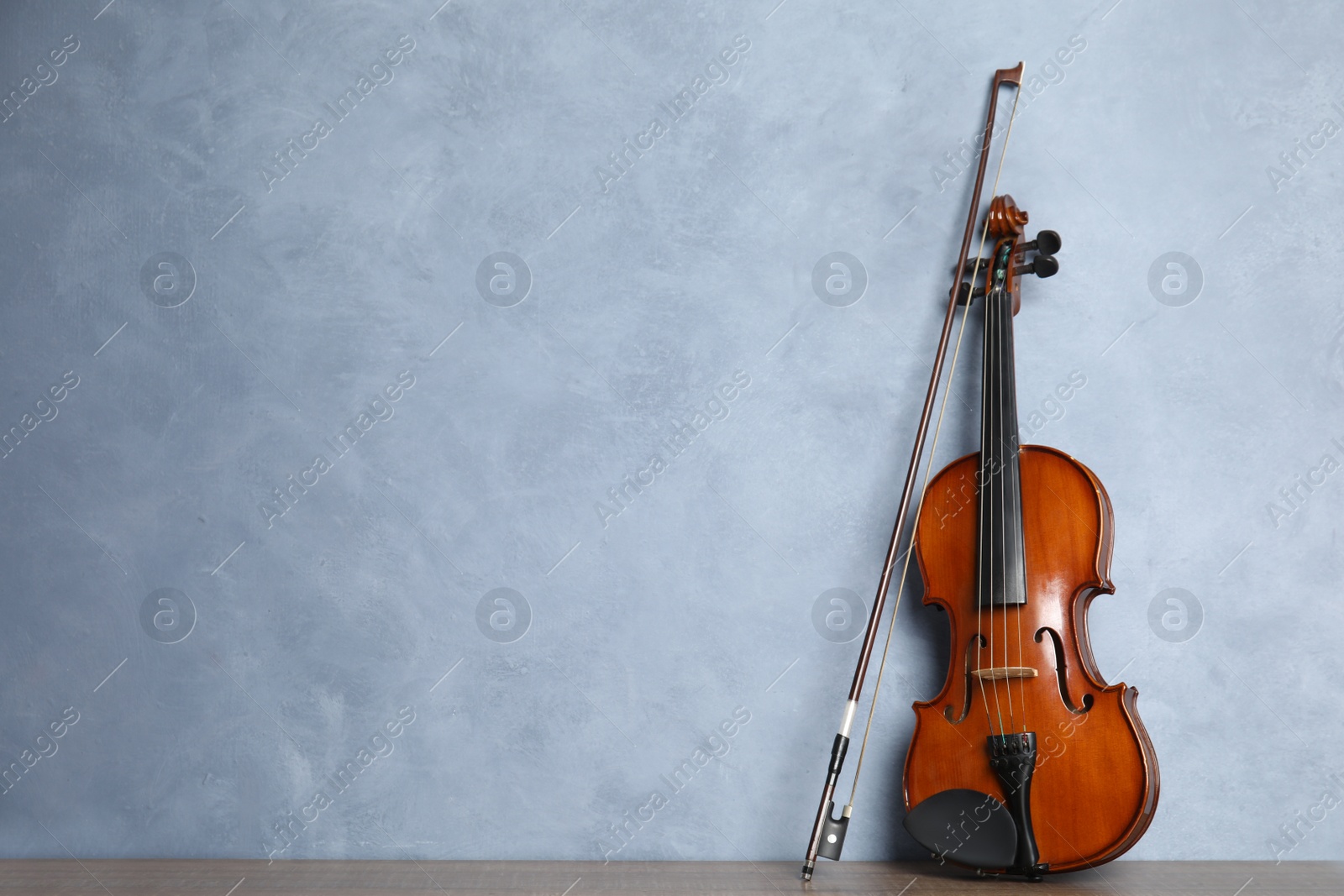 Photo of Beautiful violin and bow on wooden table near light blue wall. Space for text