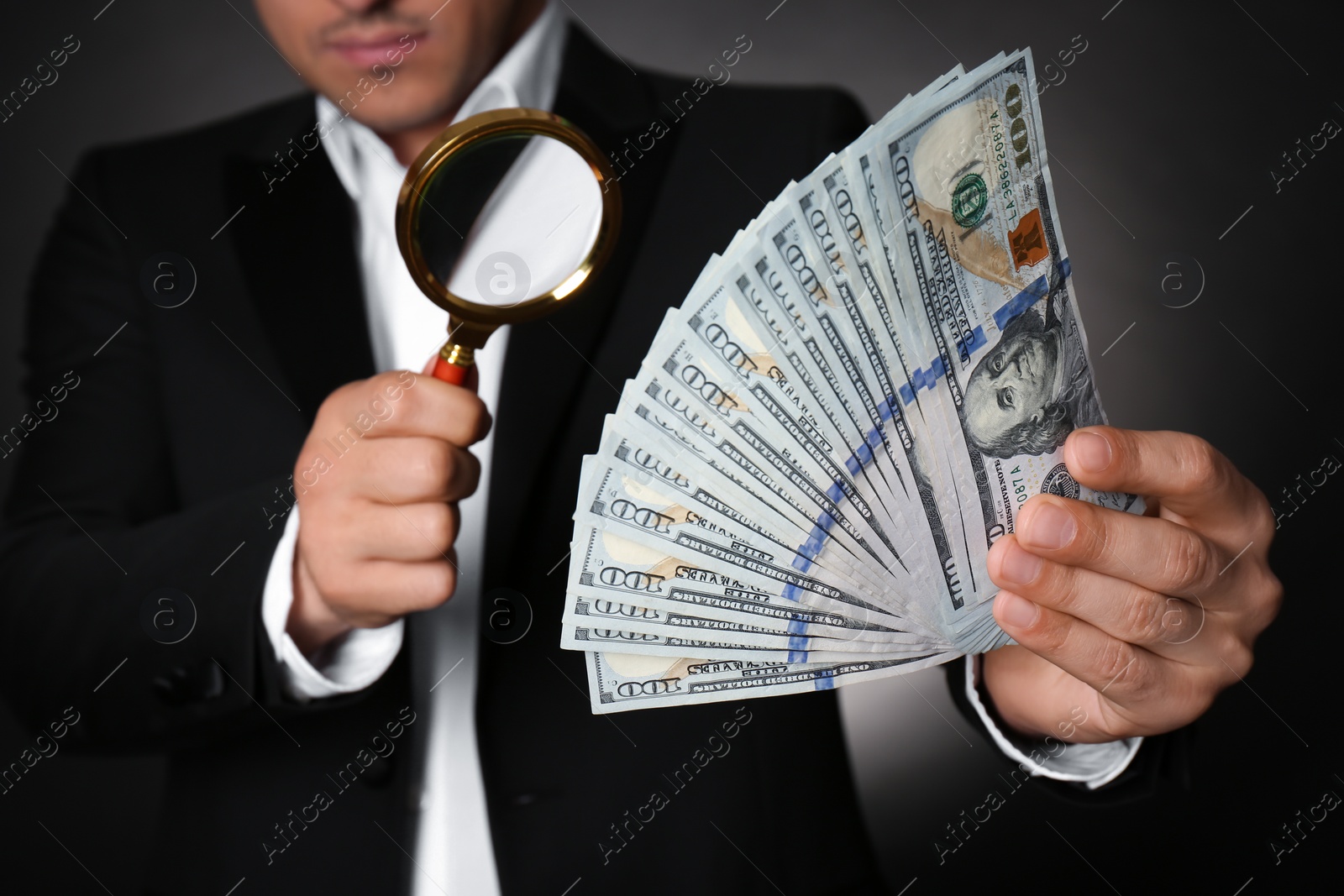 Photo of Expert authenticating 100 dollar banknotes with magnifying glass against dark background, closeup. Fake money concept