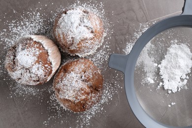 Photo of Sieve with sugar powder and muffins on grey textured table, flat lay