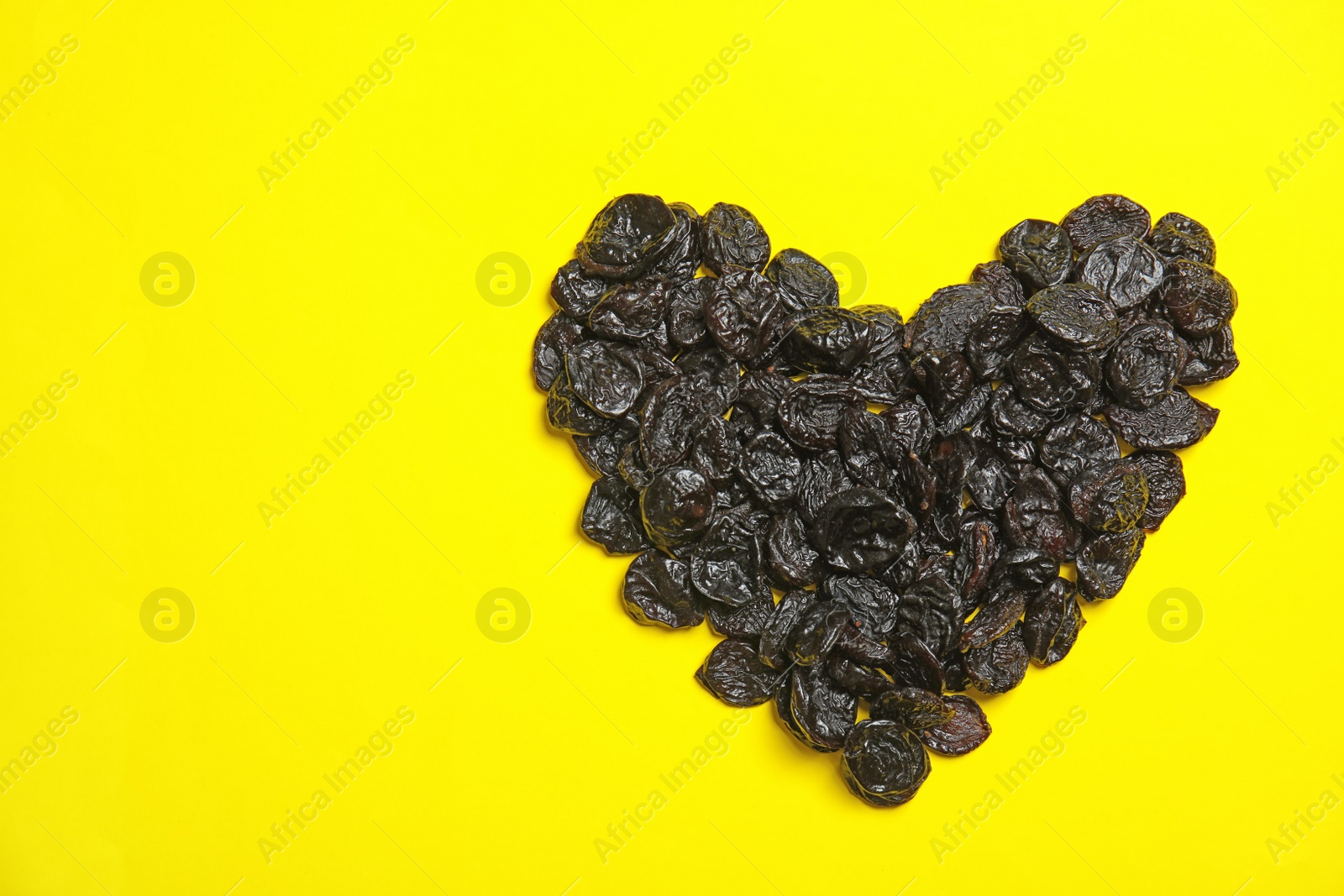 Photo of Heart shaped heap of tasty prunes on color background, top view with space for text. Dried fruit as healthy snack