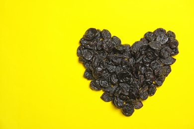 Heart shaped heap of tasty prunes on color background, top view with space for text. Dried fruit as healthy snack