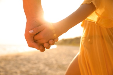 Lovely couple holding hands on beach at sunset, closeup