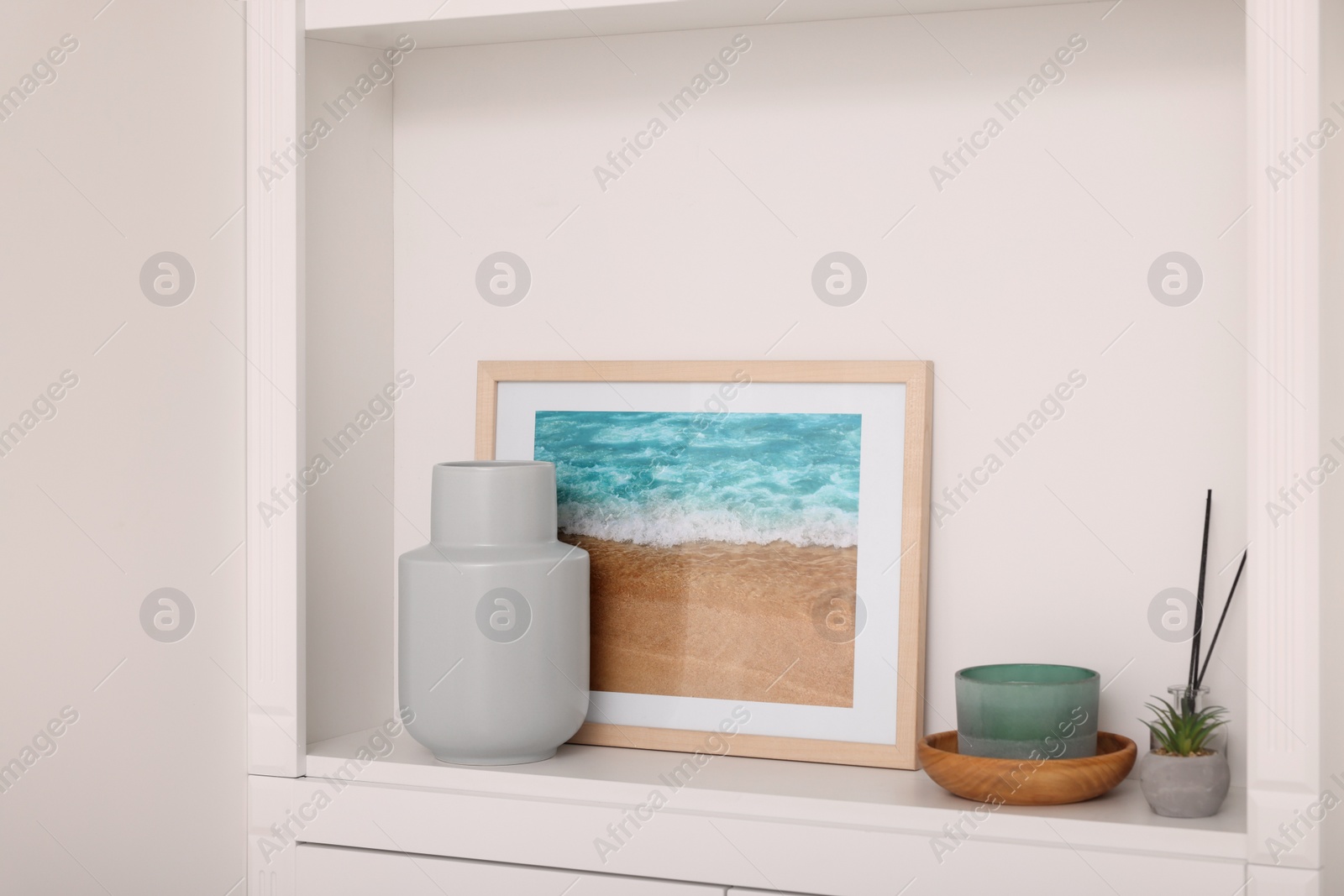 Photo of Interior design. Shelf with stylish accessories, potted plant and picture near white wall