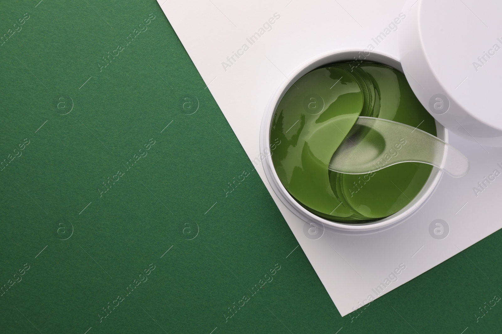 Photo of Jar of under eye patches with spoon on color background, top view and space for text. Cosmetic product