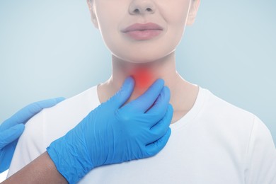 Endocrinologist examining thyroid gland of patient on light blue background, closeup