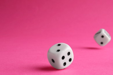 Photo of Two white game dices falling on pink background, closeup. Space for text