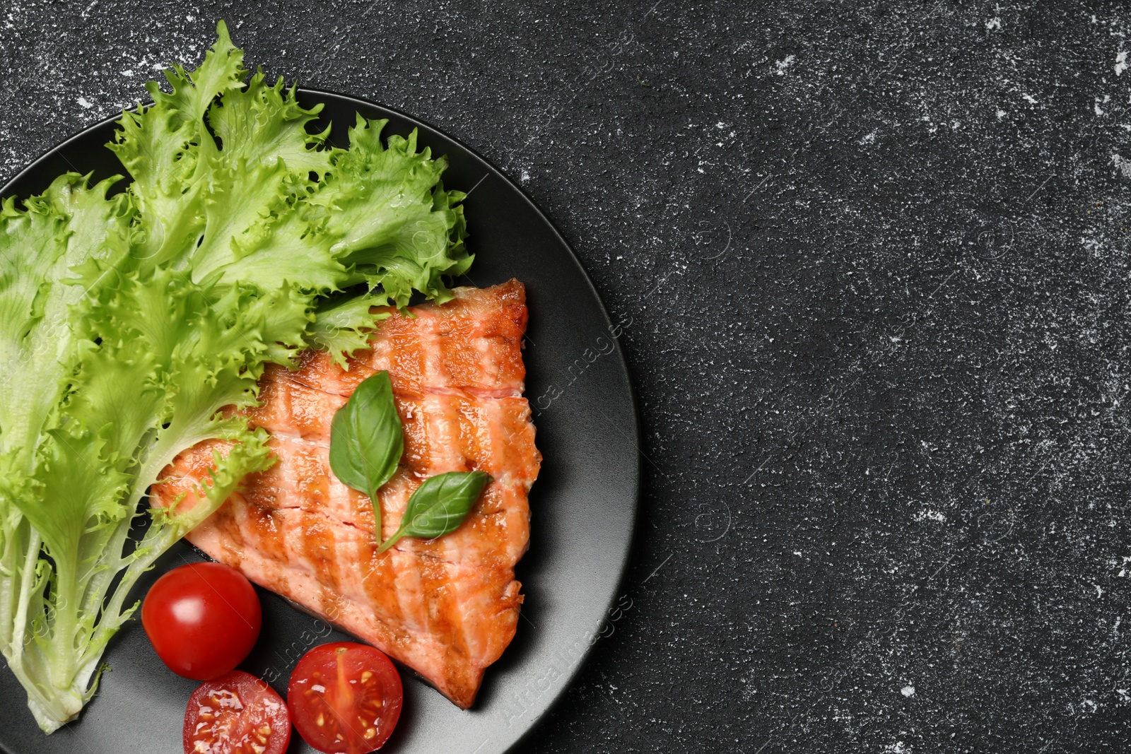 Photo of Tasty grilled salmon with tomatoes and fresh lettuce on black table, top view. Space for text