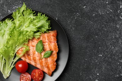 Photo of Tasty grilled salmon with tomatoes and fresh lettuce on black table, top view. Space for text