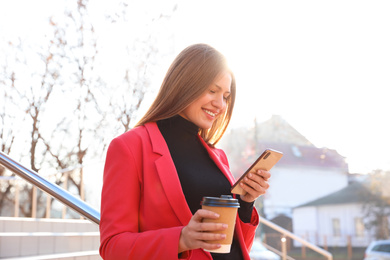 Photo of Businesswoman with cup of coffee and smartphone on city street in morning